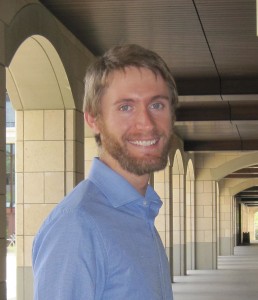 Greg poses for a photo in an outdoor hallway 